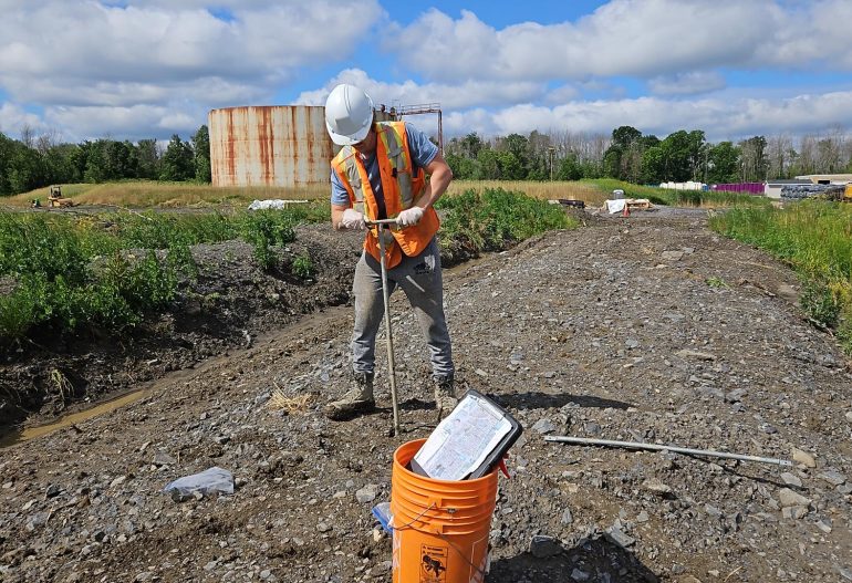 Environmental scientist collecting surface soil samples from a bioremediation biopile with a hand auger